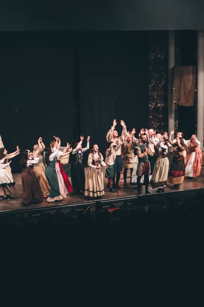 A theatre ensemble reaching upward together on stage